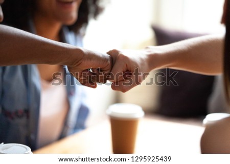 Close up multiracial best friends fist bumping, greeting each other, students celebrating successful exam results together, sitting in cafe, drinking coffee, symbol giving respect Royalty-Free Stock Photo #1295925439