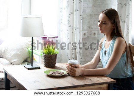 Alone pensive young woman sitting at table and drinking coffee in cafe, attractive thoughtful girl thinking about future, waiting, having breakfast in restraint, holding cardboard cup in hands Royalty-Free Stock Photo #1295927608