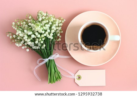 Lily of the valley - spring flowers with empty tag and cup of coffee on pastel pink background. Mothers Day, birthday, Valentines Day, Woman's Day, morning coffee concept. Top view, flat lay. 