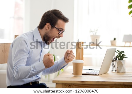 Euphoric happy businessman scream read good online news celebrating business success, great result watching game on laptop, excited by victory, betting win, professional achievement, feeling winner Royalty-Free Stock Photo #1296008470