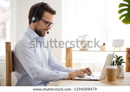 Smiling businessman in headset working on laptop make conference video call using computer, friendly professional operator salesman consulting client online, customer service support helpline concept Royalty-Free Stock Photo #1296008479