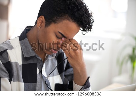 Tired african woman taking off glasses feel eye strain massaging nose bridge, fatigued black girl suffer from discomfort tension problem after long wearing glasses computer work, bad vision concept Royalty-Free Stock Photo #1296008506