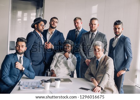 Group of multiethnic smart male professionals in formalwear with Middle eastern ethnicity investor sitting at mail in centre