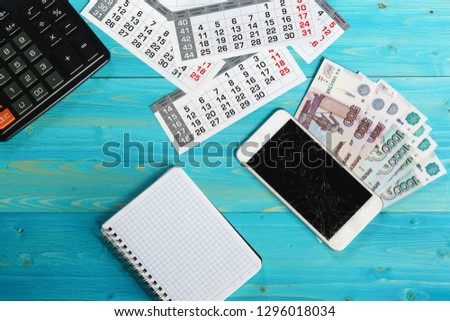 Calendar, broken smartphone and Russian money on a blue wooden table. Unforeseen expenses have disrupted plans