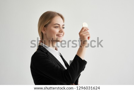 A woman in a shirt and a dark jacket holds a coin in her hand and smiles                       