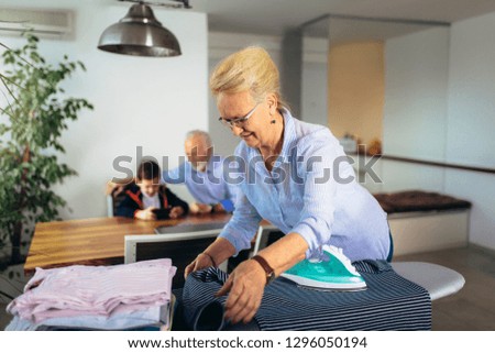 Grandma's ironing clothes, and grandfather plays with his grandson at home.