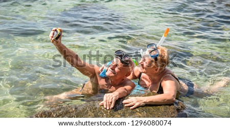Happy retired couple taking selfie in tropical sea excursion with water camera and snorkel mask - Boat trip snorkeling in exotic scenarios - Elderly concept with active seniors traveling around world
