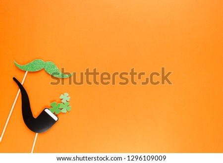 Creative st Patricks Day orange background. Flat lay composition of Irish holiday celebration with photo booth decor: hat, glasses, bow tie, lips. With Copy space, greeting card, top view