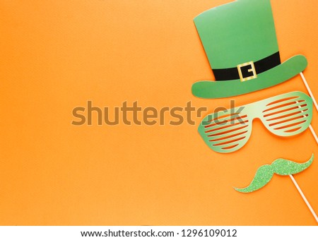 Creative st Patricks Day orange background. Flat lay composition of Irish holiday celebration with photo booth decor: hat, glasses, bow tie, lips. With Copy space, greeting card, top view Royalty-Free Stock Photo #1296109012