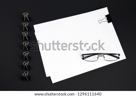 White sheets, glasses and binder clip device for tying paper sheets together on black background, top view, mock up, close up