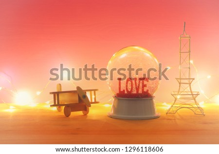 Valentine's day background. Water globe with word LOVE and glitter next eiffel tower, wooden toy plane, over the table and pink bakground