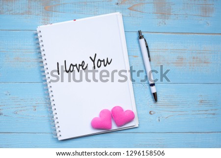 I LOVE YOU word on notebook and pen with couple pink heart shape decoration on blue wooden table background. Wedding, Romantic and Happy Valentine’ s day holiday concept