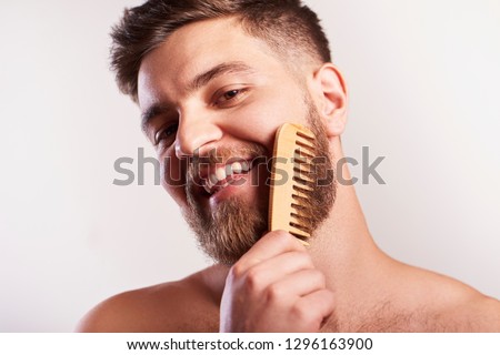 Attractive smiling Bearded man  holding a comp for beard standing above grey background Royalty-Free Stock Photo #1296163900