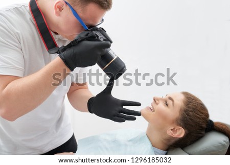 Gorgeous woman lying on dentist chair and posing. Adorable, beautiful woman showing teeth and brilliant smile after dentistry care. Photographer in black gloves taking photo.