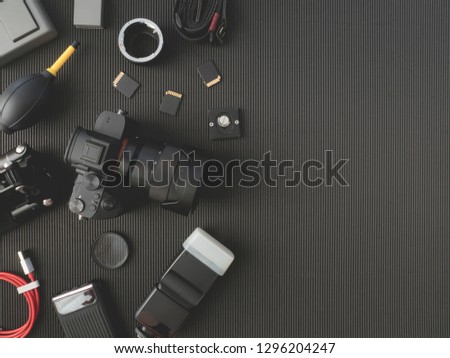 top view of work space photographer with digital camera, flash, cleaning kit, memory card and camera accessory on black table background with copy space.