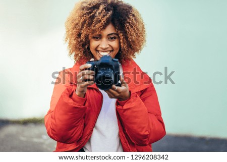 Portrait of a cheerful afro american woman holding a dslr camera. Female traveller shooting photos outdoors with a digital camera.