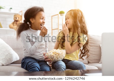 Best friends watching funny cartoon and eating popcorn, sitting on sofa at home