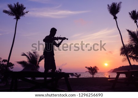 Local musicians, Asian man playing violin on the coconut beach at sunrise , Silhouette artist on purple sky background.