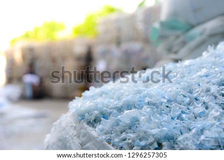 Close up PET plastic bottle flakes in white big bag with blur plastic bottle bales background  Royalty-Free Stock Photo #1296257305