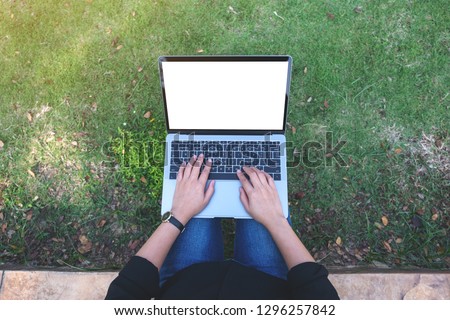 Top view mockup image of a woman using and typing on laptop with blank white screen , sitting in the outdoors with nature background
