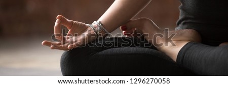 Close up female hand with bracelets fingers in Gyan mudra symbol of wisdom, girl wearing black activewear practice yoga sitting in lotus pose, banner for website header design with copy space for text Royalty-Free Stock Photo #1296270058