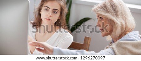 Older and younger women colleagues working on new project discuss online app point on pc screen mentor teach help intern explain corporate software, teamwork concept close up banner for website header
