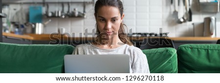 Horizontal photo focused mixed race woman sitting on couch at home using working on laptop reading news check email communicate online concept banner for website header design with copy space for text