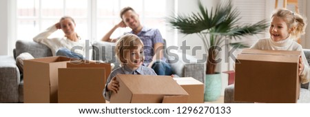 Little kids help with stuff in big carton boxes play having fun, happy parents resting on couch in living room, relocate move day at new home concept. Horizontal photo banner for website header design
