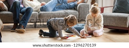 Horizontal image little kids play drawing on warm floor parents resting on couch family spend free time together, leisure activity at modern comfortable home concept, banner for website header design Royalty-Free Stock Photo #1296270139
