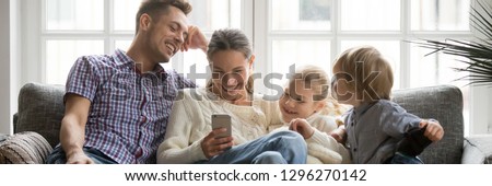 Horizontal photo happy family with little kids watching funny video on phone sitting on couch enjoy weekend at home, modern tech leisure activities free time concept, banner for website header design