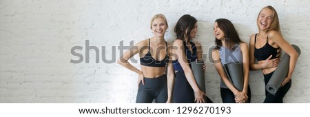 Cheerful women wearing activewear standing near wall hold yoga mats ready start fitness training sportive healthy wellbeing lifestyle concept, banner for website header design with copy space for text Royalty-Free Stock Photo #1296270193