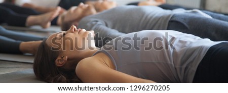 Close up focus on young woman practicing yoga lying in Savasana Corpse pose exercise at group training with girls guys in sport club wellness concept. Horizontal photo banner for website header design