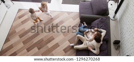 Horizontal photo above view couple resting sitting on couch, small kids play run in living room at new home, relocation and buy house concept, banner for website header design with copy space for text