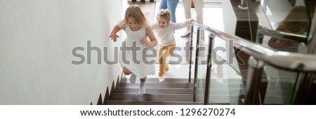 Happy kids go upstairs to second floor their new modern house, family moving day relocation and loan, buy first home concept. Horizontal photo banner for website header design with copy space for text Royalty-Free Stock Photo #1296270274