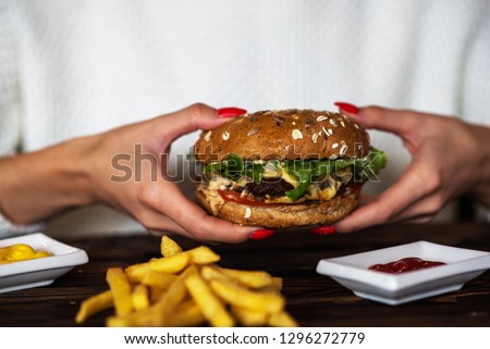 Hands holding fresh delicious burgers with french fries and sauce on the wooden table. Homemade burgers in a rustic style. Cheeseburger, with beef, tomato, cheese, cucumber and lettuce.