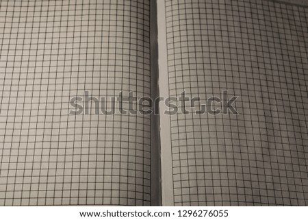 A book, a notebook with a checkered pattern on a wooden table in different poses. The cover is grey and soft with texture. Square patterns stitched with threads. Write notes in a diary. Plain white pa