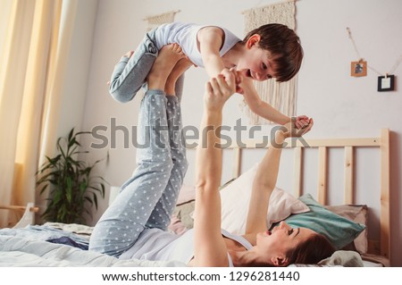 mother doing morning gymnastics with happy toddler son in bed. Happy family playing at home 