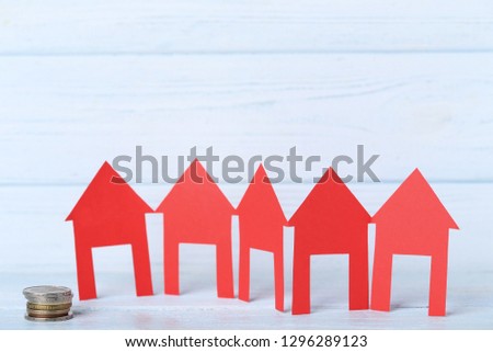 Red paper houses with coins on wooden table
