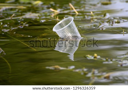 plastic cup among aquatic plants floating in green water. Concept - ecology, clean planet, planet without plastic