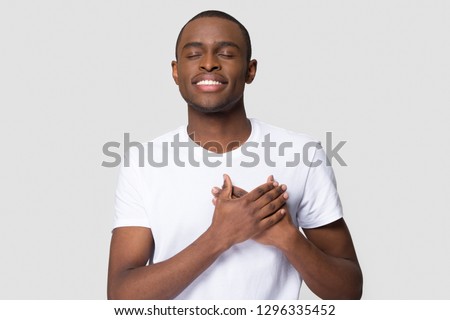 Grateful happy pleased african man holding hands on chest to heart feeling love appreciation gratitude honesty, thankful sincere proud black guy thanking isolated on white studio blank background
