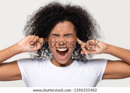 Stubborn angry annoyed black woman sticking plug fingers in ears not listening, mad african girl feel ear pain scream suffer from too loud noise sound isolated on white grey blank studio background Royalty-Free Stock Photo #1296335482