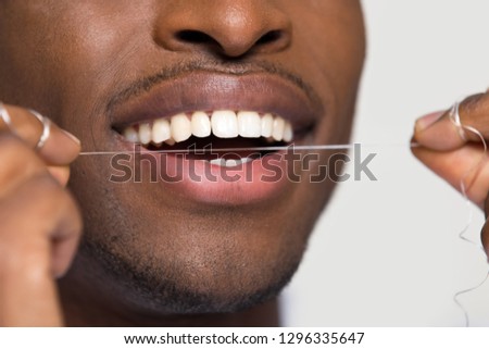 Close up view of african american black man cleaning white healthy teeth holding using dental floss isolated on grey studio blank background, oral hygiene concept, tooth health care caries prevention
