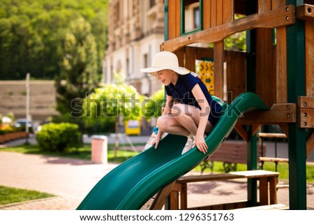 Blonde girl in the hat in the wooden house on the children playground.