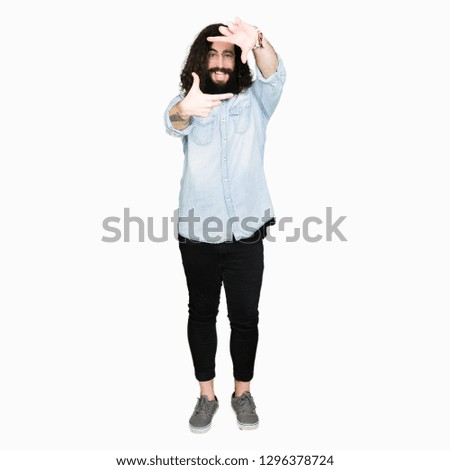 Young hipster man with long hair and beard wearing glasses smiling making frame with hands and fingers with happy face. Creativity and photography concept.