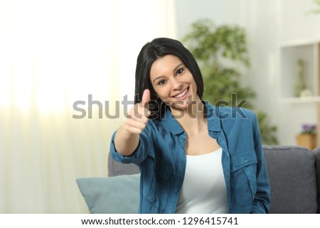 Front view portrait of a happy lady gesturing thumb up sitting on a couch at home