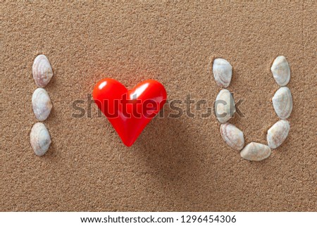 Sea shells and a red heart forming "I love you" words on a sand