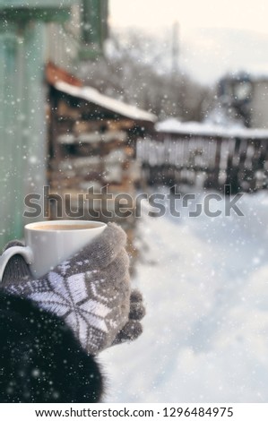 Winter picture: hands in knitted gray gloves holding a Cup of hot coffee on a snowy day on a wooden rustic background in the village. copyspace. top view