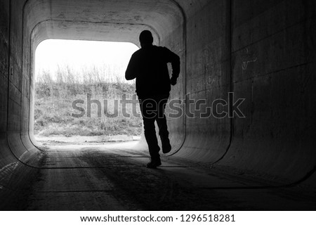 man running through dark tunnel escaping Royalty-Free Stock Photo #1296518281