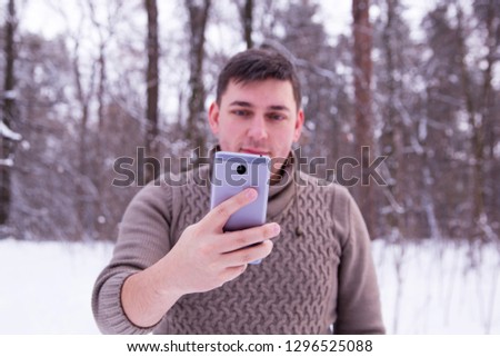man in the winter forest makes a photo on the phone. man in a sweater in the winter in the woods.