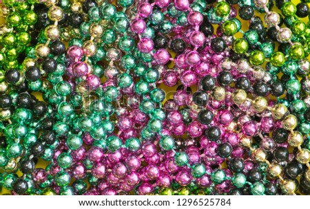 Mardi Gras beads of different colors scattered around, flat lay vibrant color splash background.